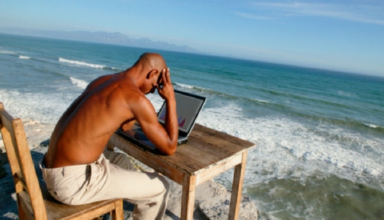 man sitting at desk with computer at a beach