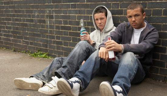 two teen boys sitting on the ground against a wall