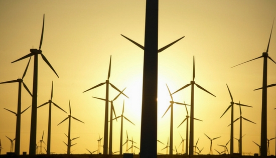 many windmills seen with the sun behind them.